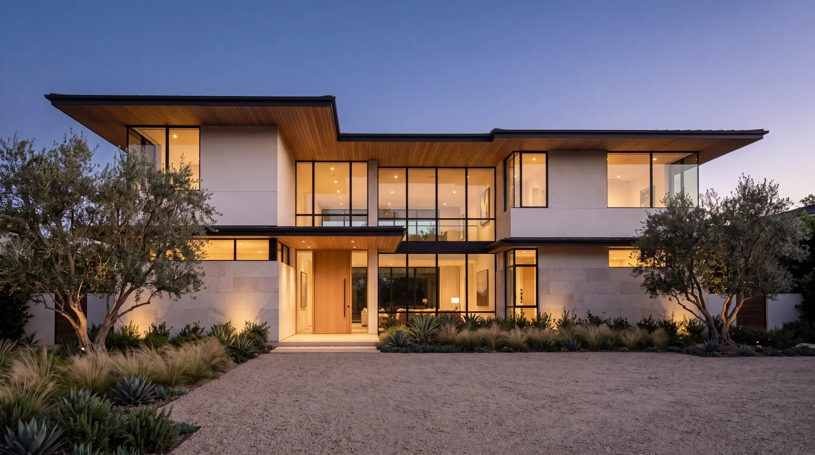 Warm contemporary two-story custom home at twilight, with wood soffits, tall glass and a gravel motor court