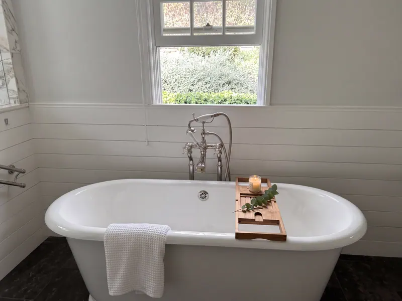 Primary bath with a freestanding tub, wall-mounted tub filler, wainscot paneling and a window above