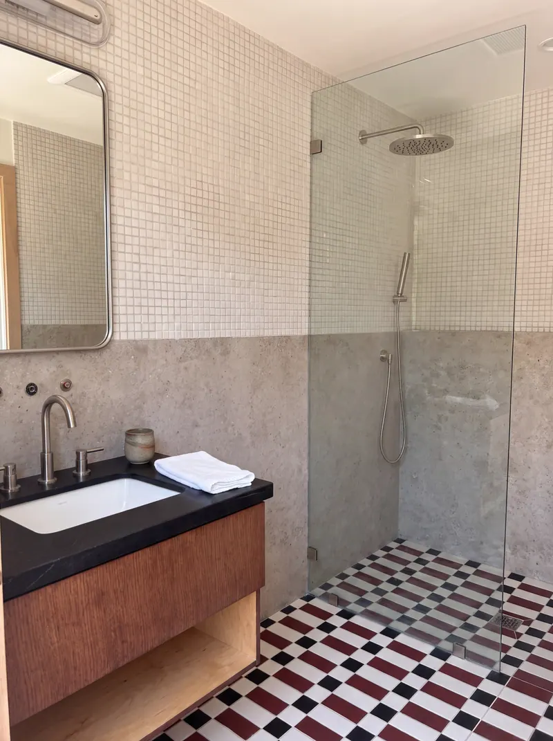 Studio bath with a checkerboard tile floor, frameless glass shower, mosaic wall tile and a walnut vanity