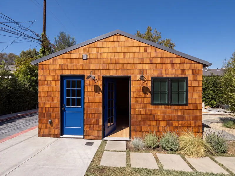 Cedar-shingle studio with a cobalt lacquered door and an open entry onto a paver walk