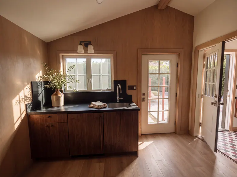 Walnut kitchenette with dark soapstone counter below a window, beside glass-paned garden doors