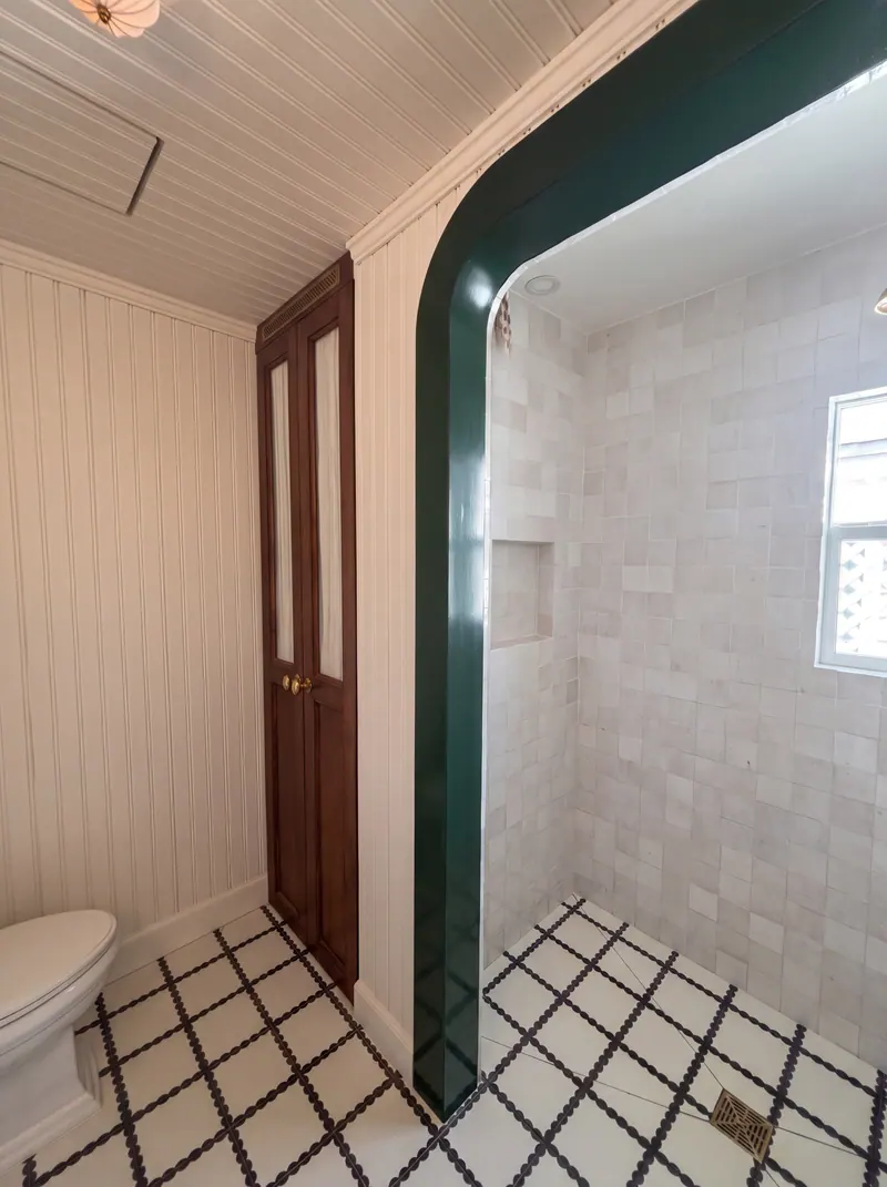 Mahogany built-in linen cabinet with reeded glass doors beside the green lacquered shower arch