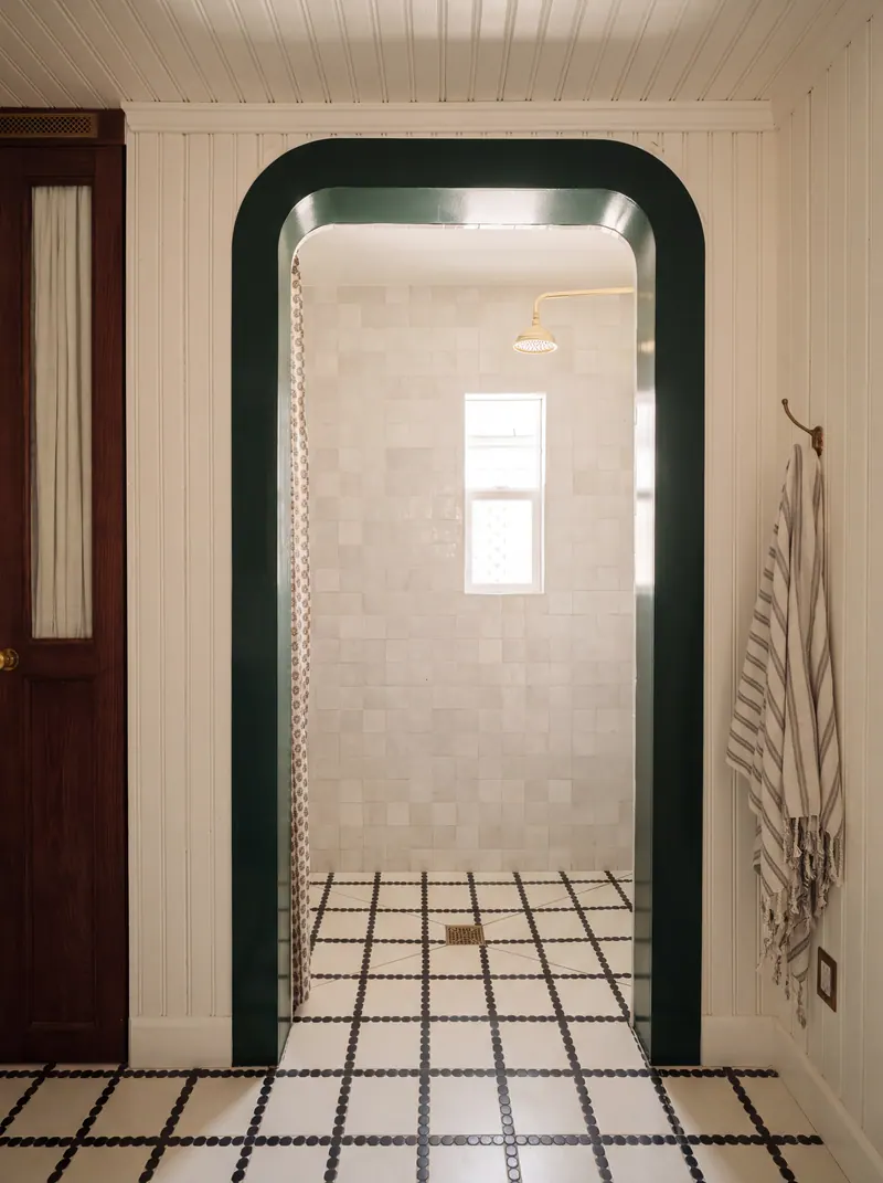 Forest-green lacquered arch opening to a white zellige shower, with a black-and-white mosaic floor