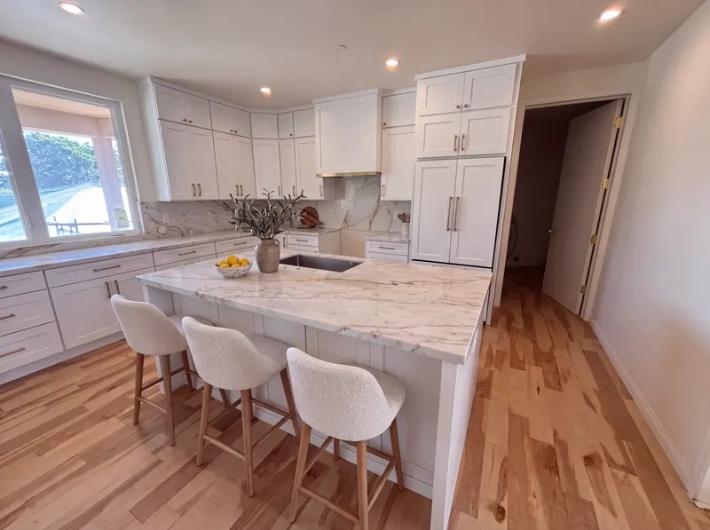 Kitchen with white shaker cabinetry to the ceiling, a range hood built into the uppers, a marble-topped island and three counter stools