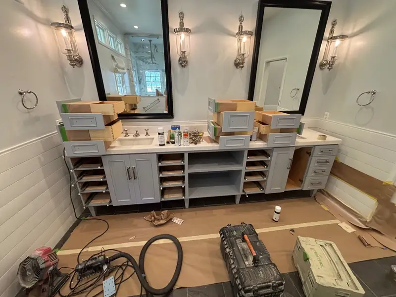 Double vanity being installed under black-framed mirrors and lantern sconces
