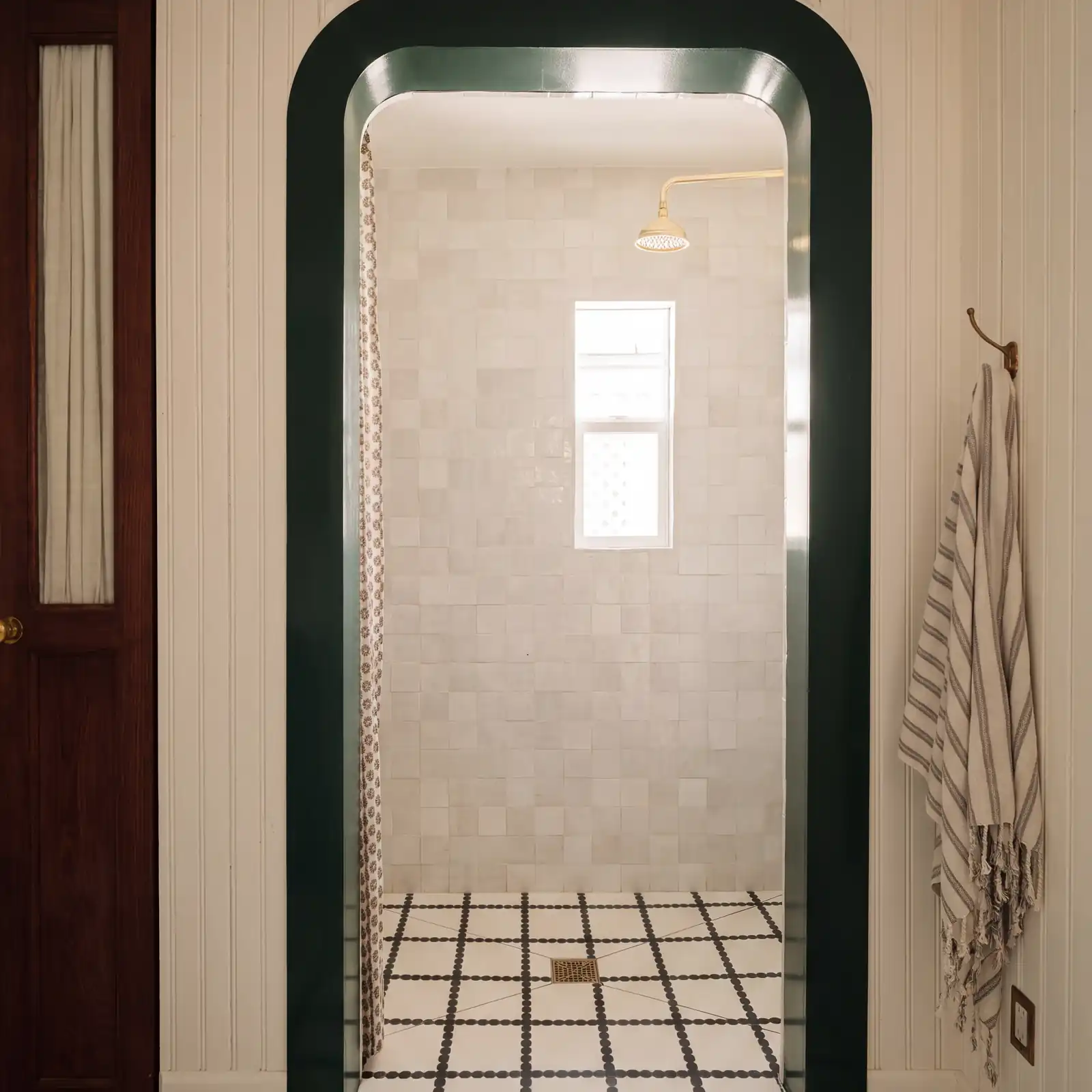 The finished shower through a green lacquered arch, with white zellige tile and a brass shower head