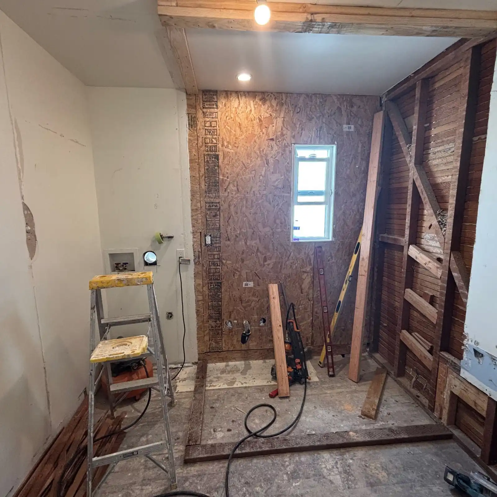 The shower wall during demolition, stripped to the sheathing around the window