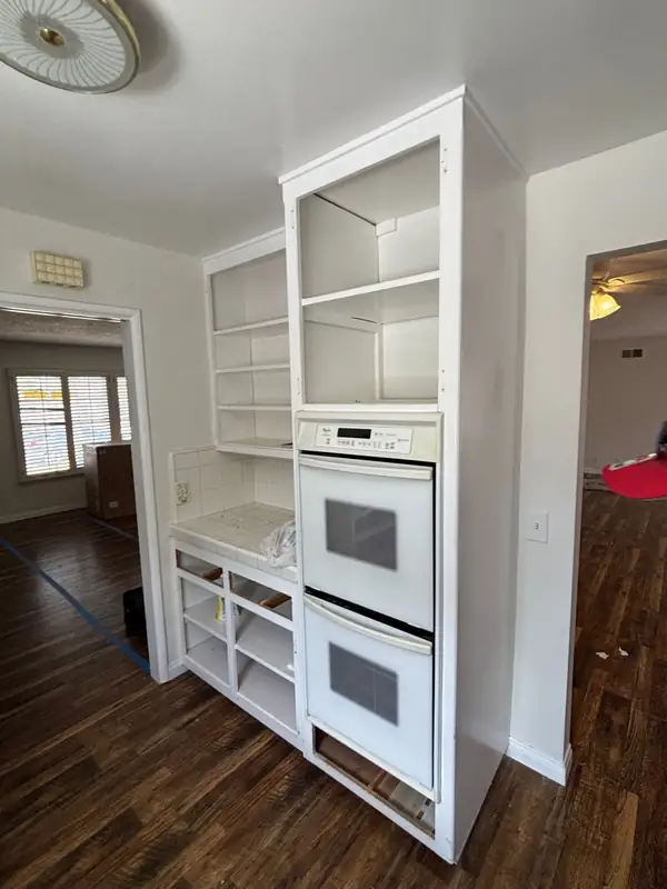 The kitchen before the remodel: white laminate cabinets, open shelving and a white wall oven