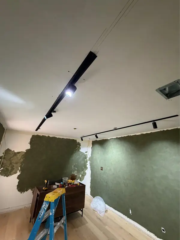 Black linear track lighting installed while the plaster wraps the walls