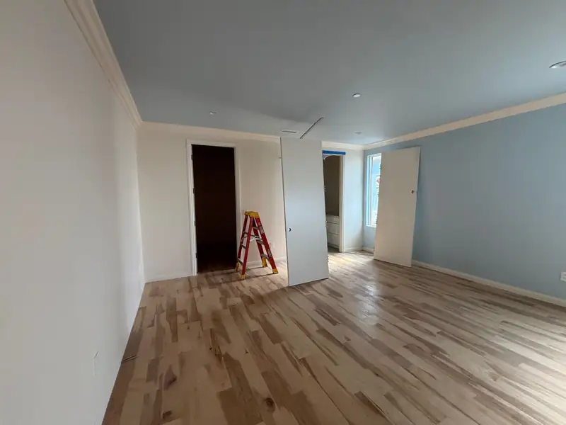 Bedroom with fresh drywall, crown molding and wide-plank wood floors, doors waiting to be hung