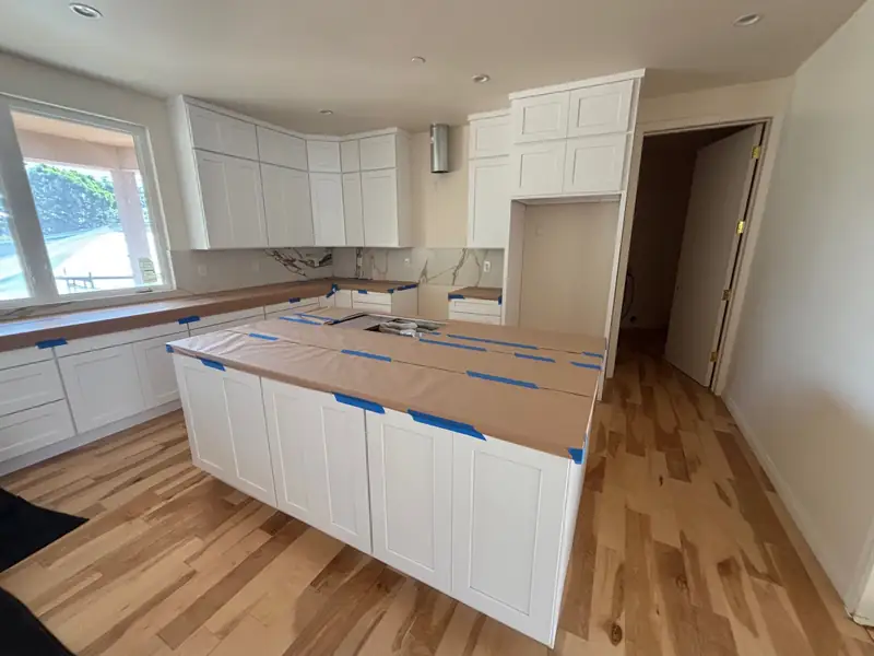 White shaker kitchen cabinetry to the ceiling around a large island, counters protected