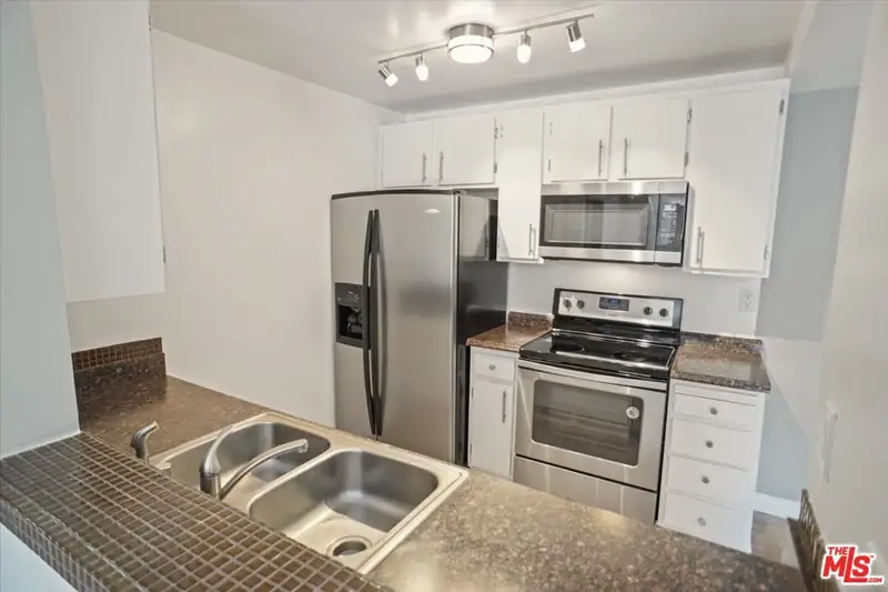 The condo kitchen before the remodel: builder-grade cabinets, tile counters and stainless appliances