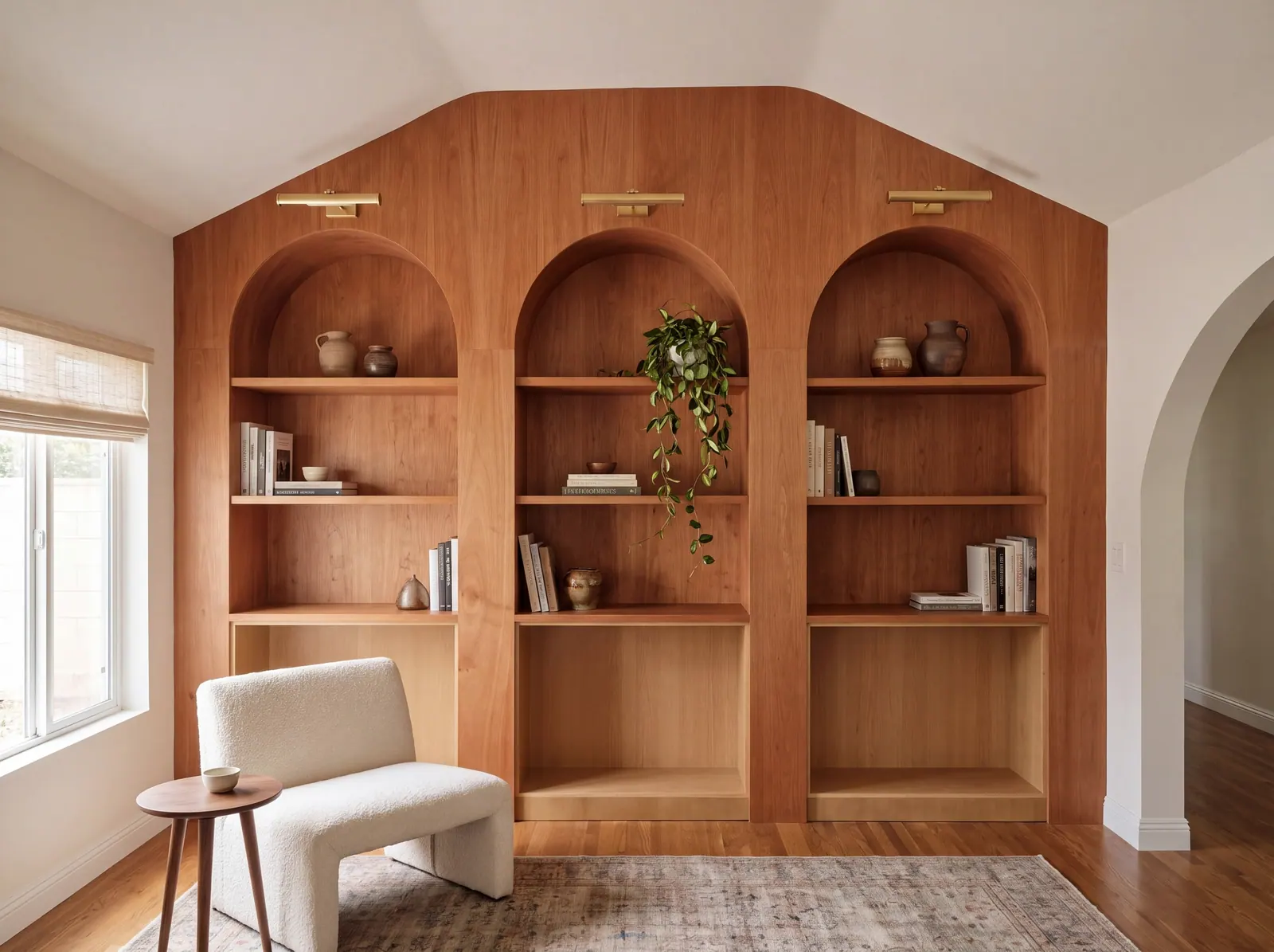 Full-height cherry built-in wall with three arched bookcases, brass picture lights and styled shelves