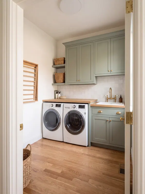 Laundry room with sage cabinetry, a butcher-block counter over the washer and dryer and a brass faucet