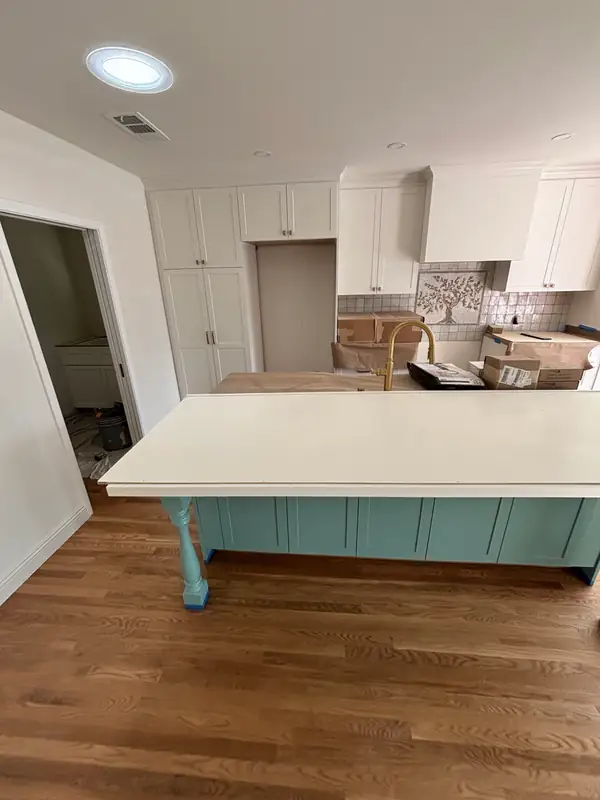 Teal island with turned legs and a stone top under protection, white shaker cabinetry behind