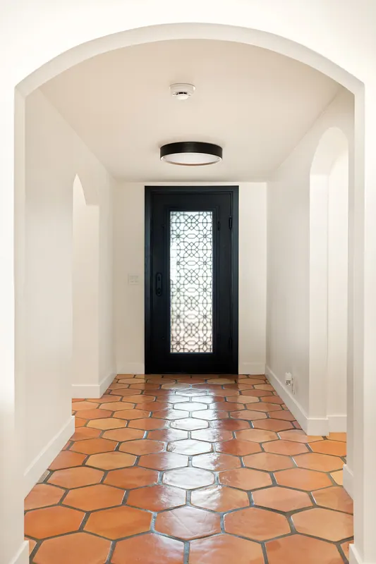 Arched entry hall with terracotta floor leading to a glass-panel front door