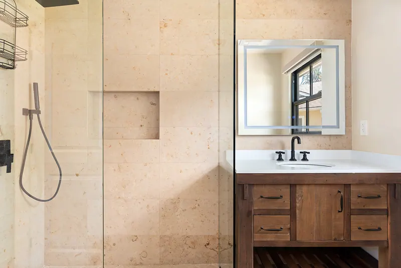 Bath with a glass shower, wood vanity and lighted mirror