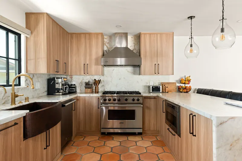 Kitchen with copper farmhouse sink, wood-grain cabinets, professional range and hexagonal terracotta floor