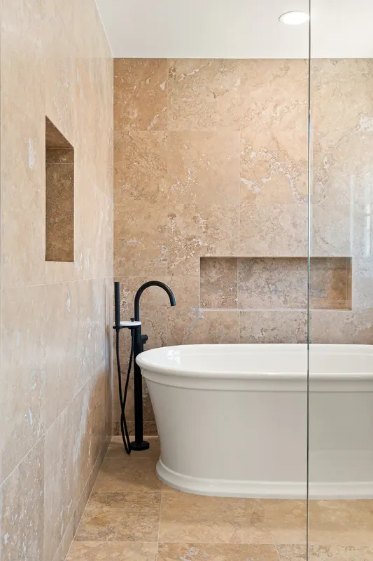 Freestanding tub in a stone-tone tile alcove with a recessed niche