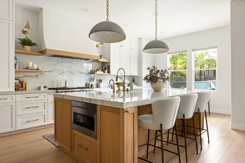 White oak kitchen island with a veined stone top, three counter stools and large pendants