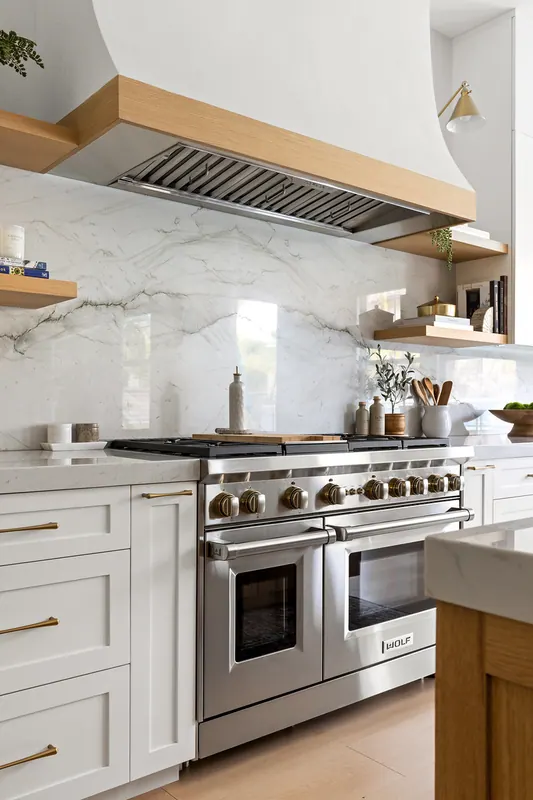 Professional range under a plaster hood with an oak shelf band and a full-height stone backsplash