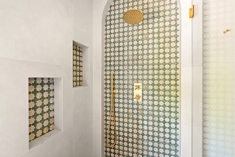 Arched shower lined with green-and-white patterned tile and brass fixtures