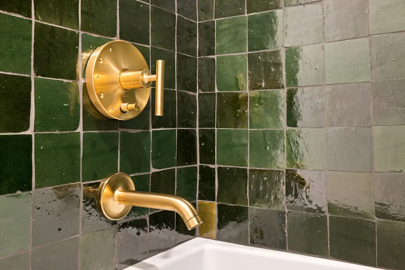 Brass wall-mounted tub filler and valve on green glazed tile