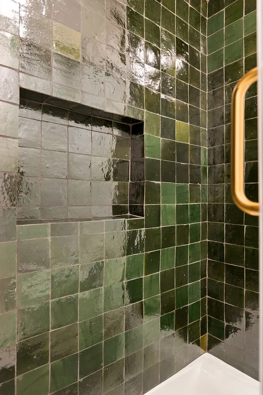 Shower wall in deep green glazed tile with brass trim