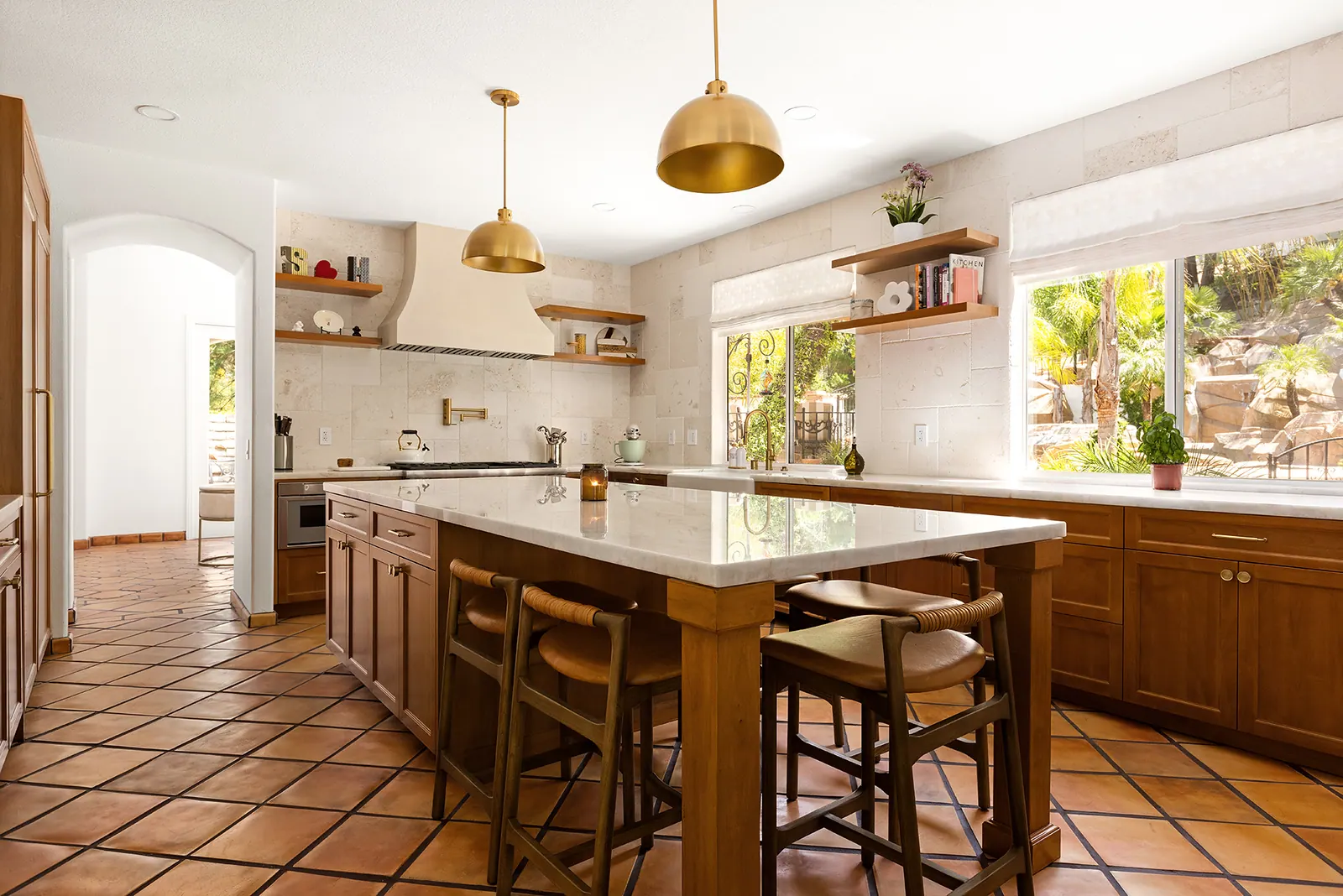 Spanish-style kitchen with a long island, brass pendants and terracotta floor tile