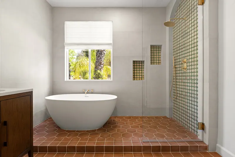 Primary bath with a freestanding tub, terracotta floor and patterned tile shower