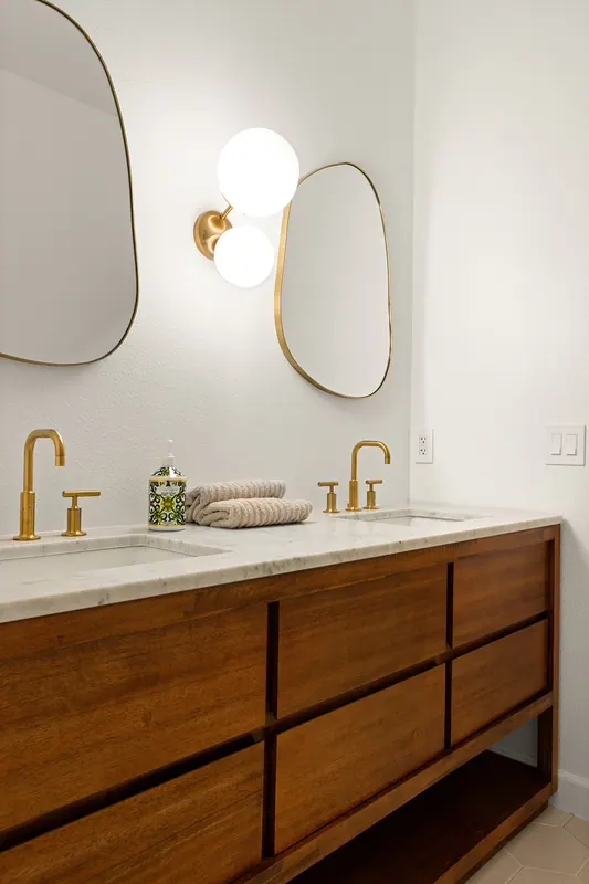 Floating walnut vanity with brass faucet and a pill-shaped mirror