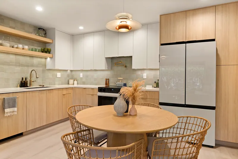Open kitchen with light oak lower cabinets, white uppers, sage tile and a round dining table